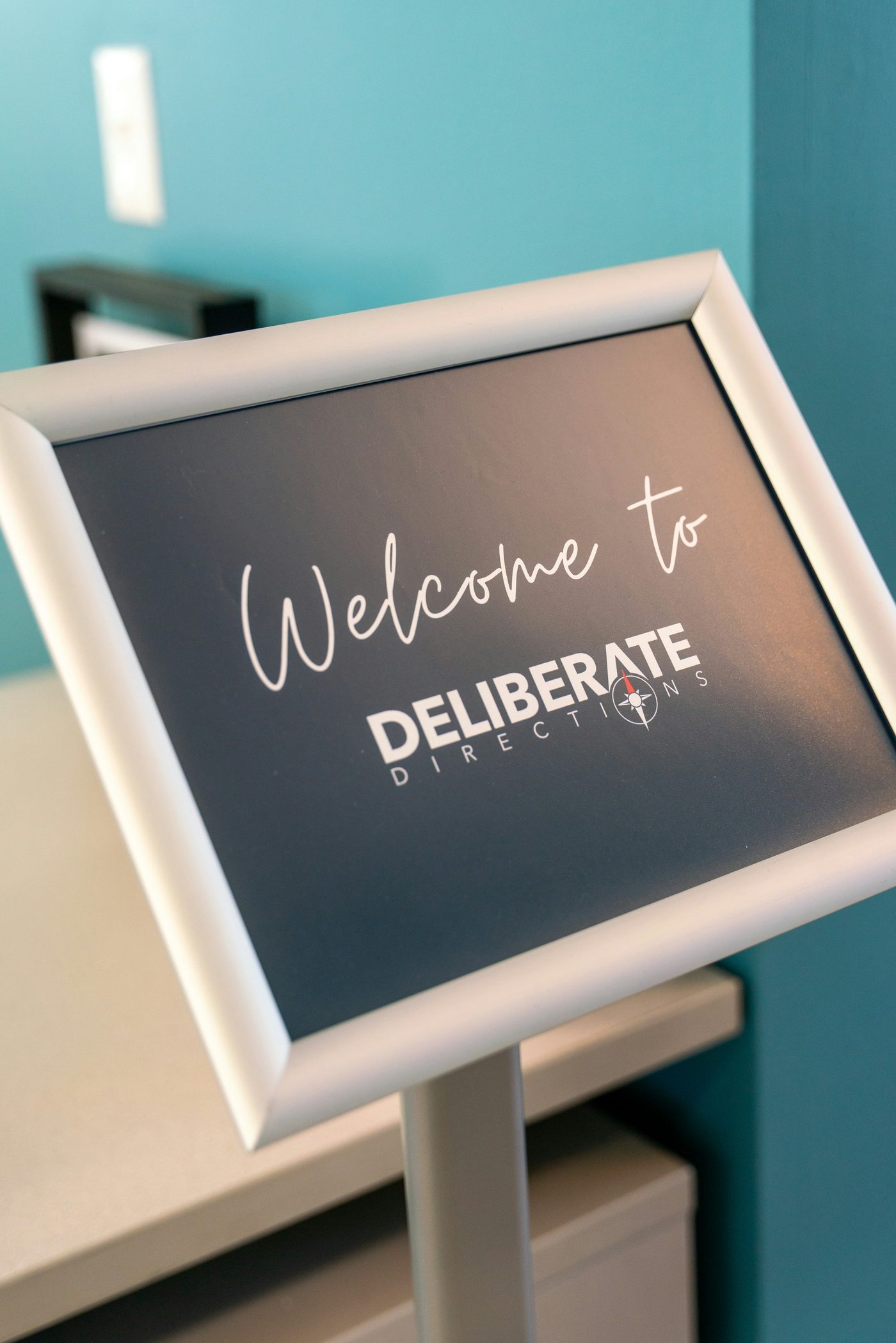 Reception welcome sign on a brushed metal A-frame stand against a teal feature wall